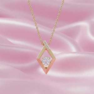 May include: A gold pendant necklace with a diamond-shaped frame and a round, clear gemstone at the center. The necklace has a delicate chain and is set against a pink background.