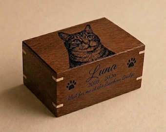 May include: A wooden pet urn with a detailed engraved image of a cat on the lid. The urn is brown with gold accents and features the name "Luna", dates, and the phrase "Wait for me at the Rainbow Bridge".