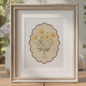 May include: A framed cross-stitch embroidery featuring a bouquet of yellow flowers with green stems and leaves, centered within a scalloped oval border on a light beige fabric background, housed in a light-colored, weathered wooden frame.
