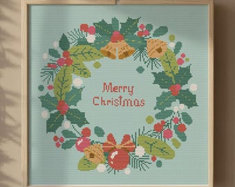 May include: A framed cross-stitch depicting a Christmas wreath with holly, berries, and bells. The wreath surrounds the words "Merry Christmas" on a light blue background. The frame is light wood, and the image is hanging on a wall with garland and fairy lights.