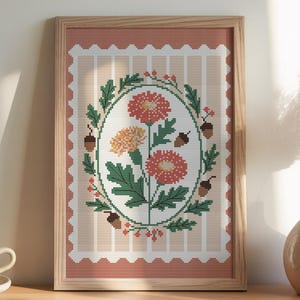 Può includere: Un design floreale a punto croce incorniciato con fiori arancioni e gialli, foglie verdi e ghiande. L'opera d'arte è ambientata su uno sfondo a righe con un bordo smerlato. La cornice è in legno chiaro.