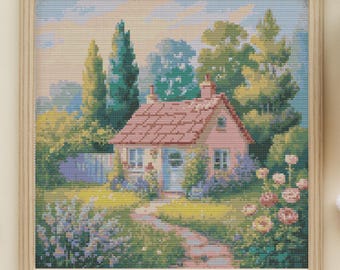Puede incluir: Un bordado enmarcado representa un paisaje con una casita rosa de tejado rojo, rodeada de vegetación y flores. Hilos de bordar, tijeras y una taza de té están dispuestos alrededor del marco, creando un tema artesanal.