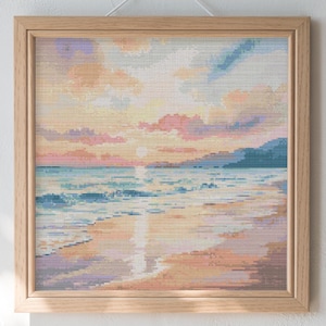 May include: A framed cross-stitch artwork showing a beach scene at sunset. The artwork features a colourful sky with pink, orange, and blue hues, reflecting on the water. The frame is made of light-coloured wood, and it hangs on a white wall.