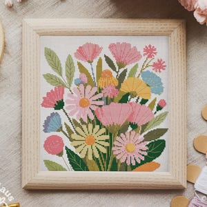 Könnte beinhalten: Ein gerahmtes Kreuzstich-Blumendesign mit einem Bouquet aus rosa, gelben und blauen Blumen mit grünen Blättern. Das Kunstwerk befindet sich in einem hellen Holzrahmen. Stickgarn und Stickrahmen umgeben die gerahmte Kunst.