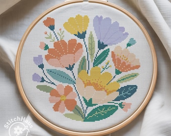Könnte beinhalten: Ein fertiges Kreuzstich-Blumendesign in einem hölzernen Stickrahmen. Das Design zeigt einen Strauß bunter Blumen in Orange, Gelb, Lila und Rosa, mit grünen Blättern. Der Text "StitchHaus Studio" befindet sich unten links.