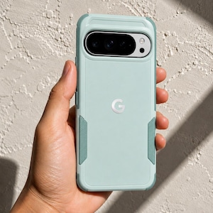 Puede incluir: Una funda para smartphone de color verde menta claro con un diseño de dos tonos, que presenta acentos texturizados en verde más oscuro en los laterales y una prominente abertura horizontal para la cámara en la parte superior. Logo G plateado.