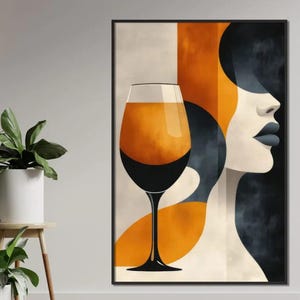 May include: Abstract art print showing a wine glass filled with amber liquid, set against a backdrop of geometric shapes in orange, black, and cream. A stylized female profile is also depicted. The artwork is framed in black.