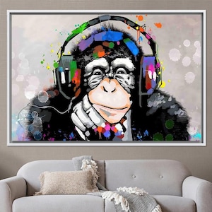 Peut inclure: Impression sur toile encadrée représentant un chimpanzé coloré portant un casque audio, dans un style pop art. Le chimpanzé a des poils noirs, un visage blanc et des éclaboussures de peinture colorées. Le casque est également coloré.