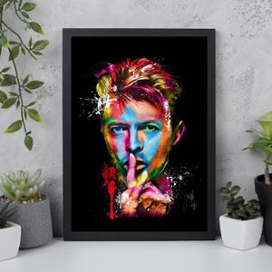 Puede incluir: Un retrato enmarcado de una persona con pinceladas coloridas sobre un fondo negro. La cara está pintada con tonos azules, amarillos, rojos y verdes. La persona se lleva un dedo a los labios en un gesto de 'shhh'.