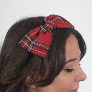 May include: A red plaid bow headband. The bow features a classic tartan pattern with red, green, yellow, and white lines. The headband is a stylish hair accessory.