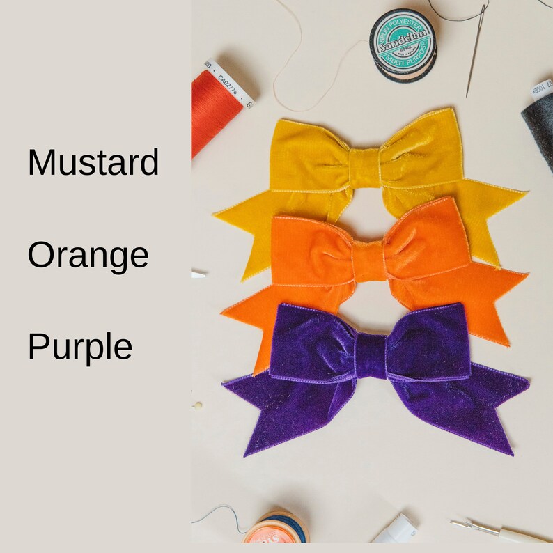 May include: Three velvet bows in mustard, orange, and purple colors. The bows are stacked on top of each other, with the mustard bow on top.