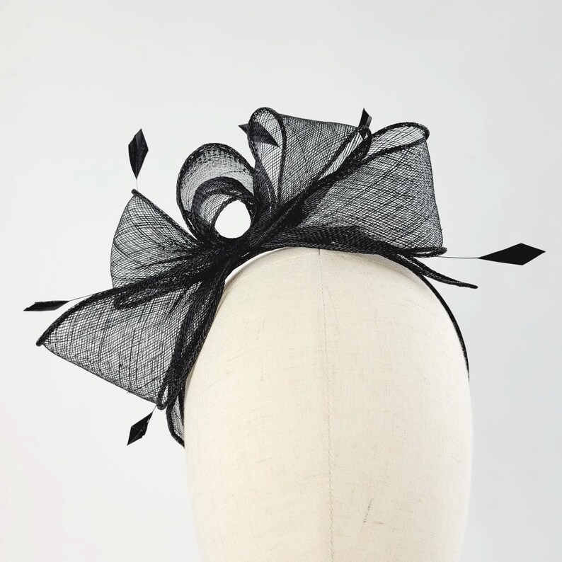 May include: Black mesh headband with a large bow and feather accents.