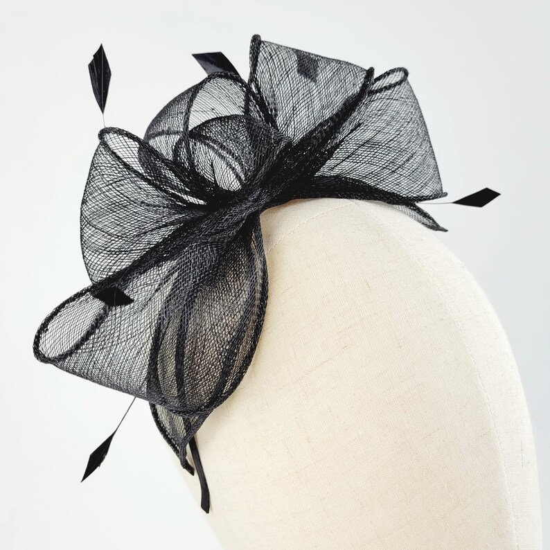 May include: Black mesh hair comb with a large bow and feathers. The comb is on a white mannequin head.