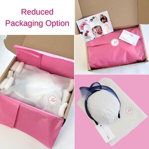 May include: A close-up of a hat in a pink tissue paper-lined box. The hat is a navy blue and white headband with a large bow. The box is labeled "Reduced Packaging Option".