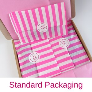 May include: A pink and white striped tissue paper with a small logo in a circle. The tissue paper is inside a brown cardboard box. The text "Standard Packaging" is at the bottom of the image.