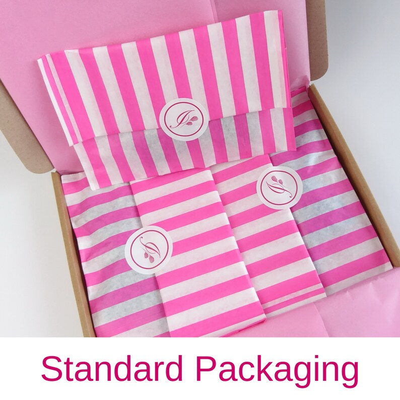 May include: A pink and white striped tissue paper with a small logo in a circle. The tissue paper is inside a brown cardboard box. The text "Standard Packaging" is at the bottom of the image.