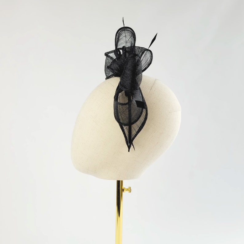 May include: A black feather hair comb with a delicate, intricate design. The comb is displayed on a white mannequin head.