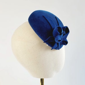 May include: A blue felt beret with a large blue felt flower accent. The beret is on a white mannequin head.