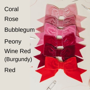 May include: Six velvet bows in shades of red, pink, and coral. The bows are arranged in a vertical stack, with the darkest red bow at the bottom and the lightest coral bow at the top. The bows are labeled with their corresponding colors: Red, Wine Red (Burgundy), Peony, Bubblegum, Rose, and Coral.