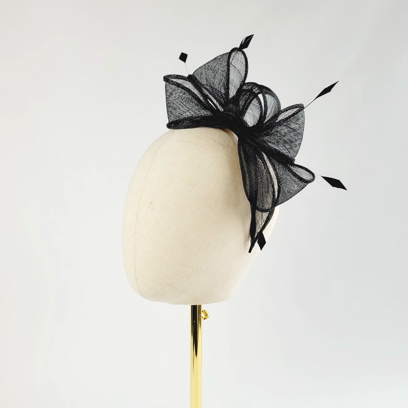 May include: A black mesh hair bow with a large, layered bow and a small, delicate bow. The bow is attached to a white mannequin head.