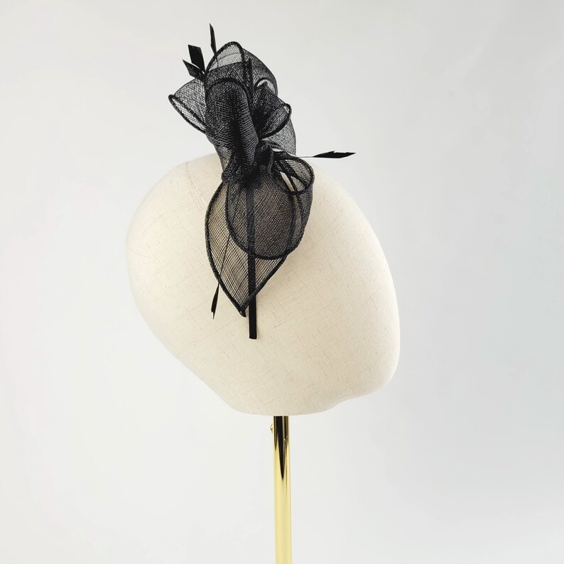 May include: Black mesh hair comb with a large bow and feathers. The comb is on a white mannequin head.