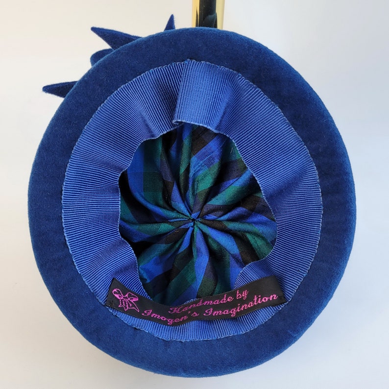 May include: A blue velvet hat with a blue ribbon and a plaid lining. The hat has a label that reads "Handmade by Imogen's Imagination".