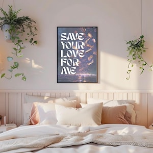 May include: A framed art print with the words "SAVE YOUR LOVE FOR ME" in white lettering. The print hangs above a bed with white bedding and decorative pillows. Green plants hang from the ceiling and on the left side of the image.