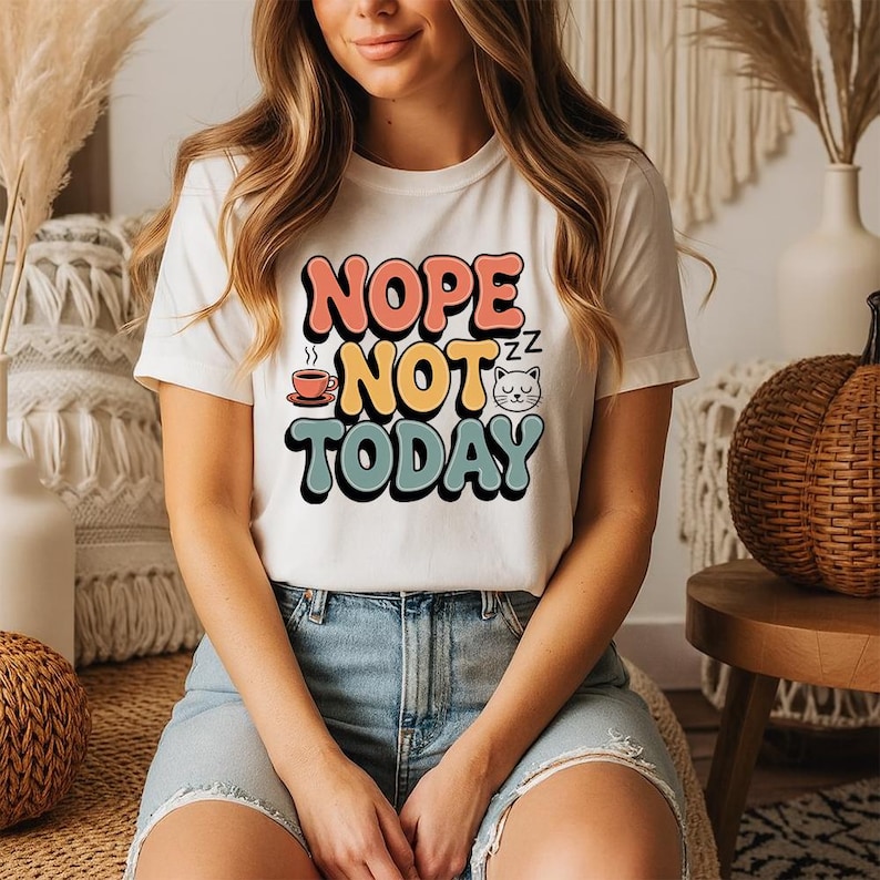 May include: A white t-shirt with the text "Nope Not Today" in a retro font. The design includes a coffee cup, a sleeping cat, and the word "Nope" in pink, "Not" in yellow, and "Today" in teal.