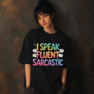May include: Black t-shirt with the text "I Speak Fluent Sarcastic" in a colorful, rainbow-gradient font. The design includes smiley face graphics. The shirt is a casual, oversized style.