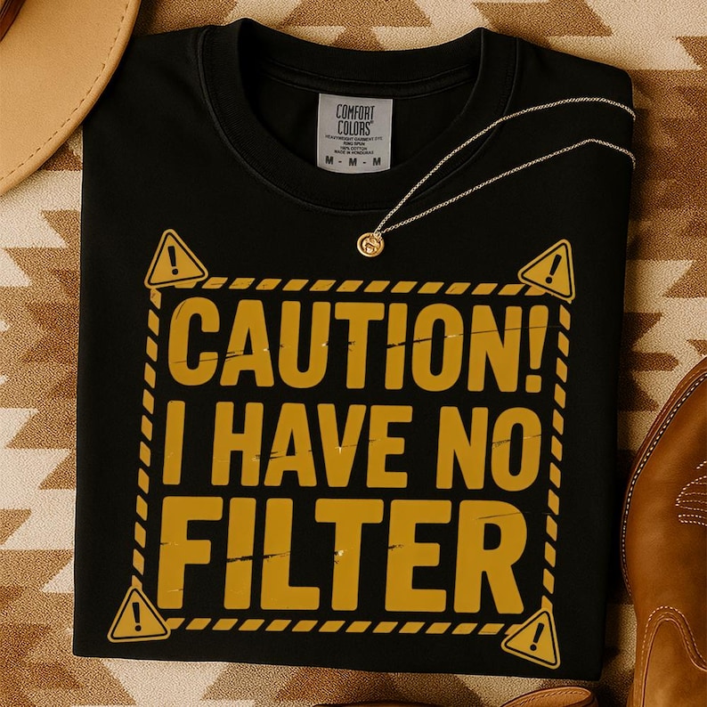 May include: Black t-shirt with the text "CAUTION! I HAVE NO FILTER" in yellow. The design includes yellow hazard symbols and a yellow border. A gold necklace is draped on the shirt.