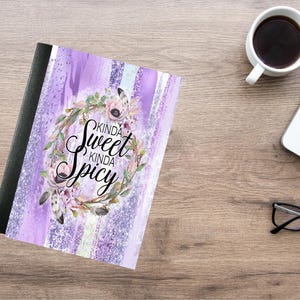 Puede incluir: Un cuaderno con un diseño de rayas moradas y blancas. La portada presenta una corona floral y el texto "Kinda Sweet Kinda Spicy". Una taza de café, un ordenador portátil y gafas también están sobre la superficie de madera.