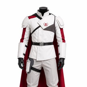 Puede incluir: Un disfraz blanco y rojo de estilo militar con una capa roja. El atuendo incluye una chaqueta blanca con detalles en negro, pantalones grises, botas blancas y guantes negros. Un emblema de calavera es visible en el pecho.