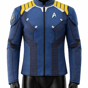 Puede incluir: Chaqueta azul con detalles amarillos y blancos, cierre de cremallera e insignia de la Flota Estelar. La chaqueta tiene paneles acolchados y cuello alto. La chaqueta se exhibe en un maniquí negro.