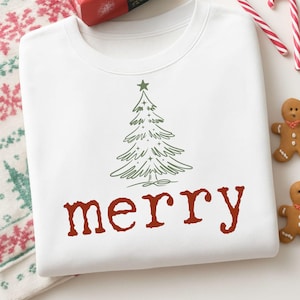 May include: White sweatshirt with a green Christmas tree graphic and the word "merry" in red. The image includes a wrapped gift, candy canes, and gingerbread men, creating a festive holiday theme.