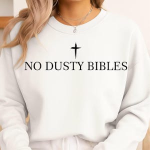May include: White sweatshirt with the text "NO DUSTY BIBLES" in black, with a black cross above the text. The sweatshirt is a crew neck style.