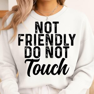 May include: White sweatshirt with the text "NOT FRIENDLY DO NOT TOUCH" in bold black letters. The sweatshirt is a crew neck style and appears to be made of a soft material. The text is centered on the front.