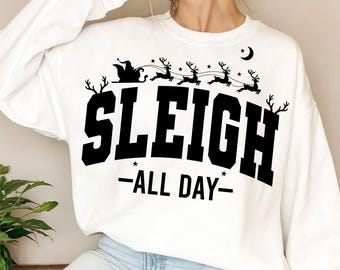 Könnte beinhalten: Weißes Sweatshirt mit schwarzer Grafik eines Schlittens, Rentieren und dem Text "SLEIGH ALL DAY". Das Design beinhaltet Sterne und einen Mond. Ein festliches Kleidungsstück für den Winter.