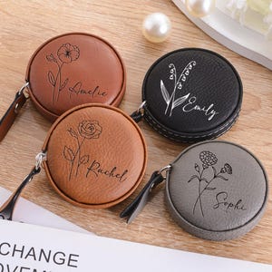 May include: Four round, personalised tape measures in brown, black, tan, and grey. Each has a floral design and a name engraved on the front. The tape measures have a black leather pull tab.