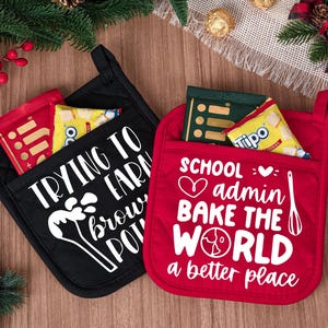 May include: Two oven mitts, one black and one red, with white text and graphics. The black mitt says "TRYING TO EARN brow POT" and the red mitt says "SCHOOL admin BAKE THE WORLD a better place."
