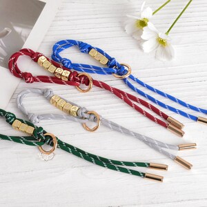 May include: Four keychains in red, blue, green, and gray with gold-colored hardware. Each keychain has a braided cord with a metallic end and a ring. Some keychains have lettered beads.
