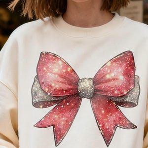 Puede incluir: Sudadera color crema con un gran lazo rojo brillante. El lazo tiene detalles plateados y un efecto brillante, creando un diseño festivo. Una parte superior cómoda y elegante.