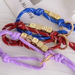 May include: Close-up of three dog collars in blue, red, and purple. Each collar features a rope design with gold-colored cube beads and a metal ring. The blue collar has white accents, the red has white accents, and the purple has a star pattern.