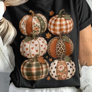 May include: A black short-sleeve t-shirt featuring a graphic print of six pumpkins arranged in two rows. The pumpkins display various patterns including floral, plaid, heart, leopard print, and polka dot designs, accented with small orange leaves.