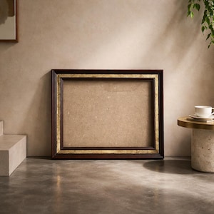 Op de afbeelding: Een rechthoekige fotolijst met een donkerbruin houten frame en gouden rand. Het frame is leeg, met een neutrale achterkant. Het frame ligt op een grijs oppervlak.