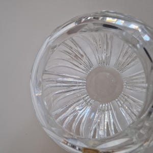 May include: Clear crystal bowl with a circular design. The bowl features a spiral pattern radiating from the center, creating a textured effect. The rim has a rounded shape, and the glass reflects light, showcasing its clarity.