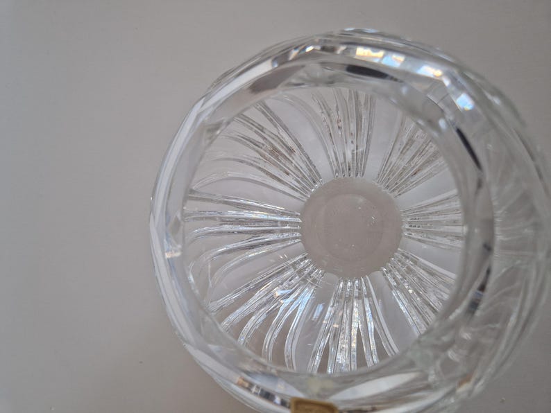 May include: Clear crystal bowl with a circular design. The bowl features a spiral pattern radiating from the center, creating a textured effect. The rim has a rounded shape, and the glass reflects light, showcasing its clarity.