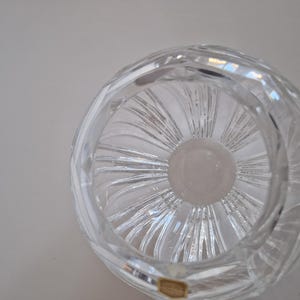 May include: Clear crystal bowl with a spiral design. The bowl has a circular shape with a thick, textured rim. The interior features a central, circular base with radiating lines. A small, rectangular sticker is visible on the bottom.