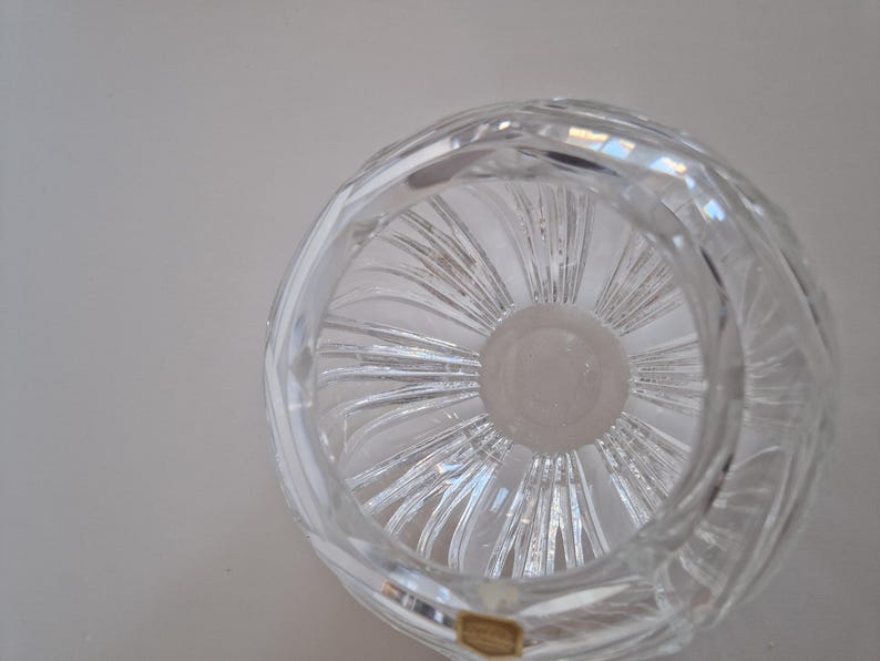 May include: Clear crystal bowl with a spiral design. The bowl has a circular shape with a thick, textured rim. The interior features a central, circular base with radiating lines. A small, rectangular sticker is visible on the bottom.