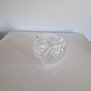 May include: A clear, spherical glass bowl with a textured, leaf-like pattern. The bowl is sitting on a white surface, and the light creates shadows that highlight the intricate design. The bowl is likely for decorative purposes.