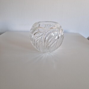 May include: A clear, round glass vase with a textured, leaf-like pattern. The vase is sitting on a white surface. The vase is likely used for decorative purposes.